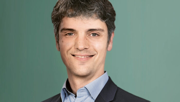 Dr. Ullmer Ein Mann im Anzug lächelt vor einem schlichten grünen Hintergrund.