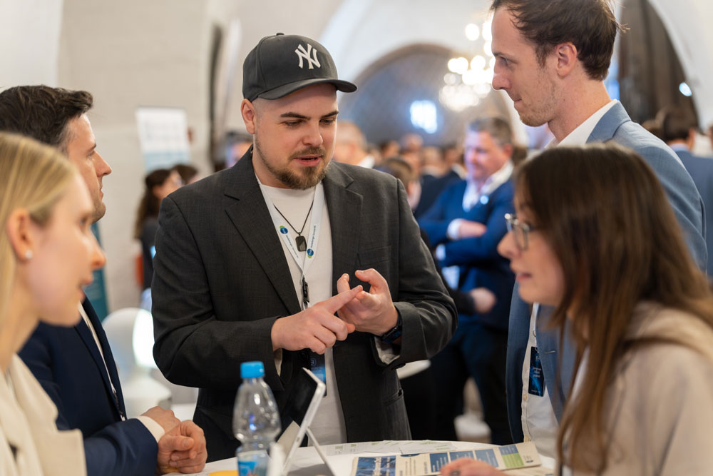 hsag-116 Vier Personen in Geschäftskleidung unterhalten sich bei einer geschäftigen Networking-Veranstaltung an einem Tisch.