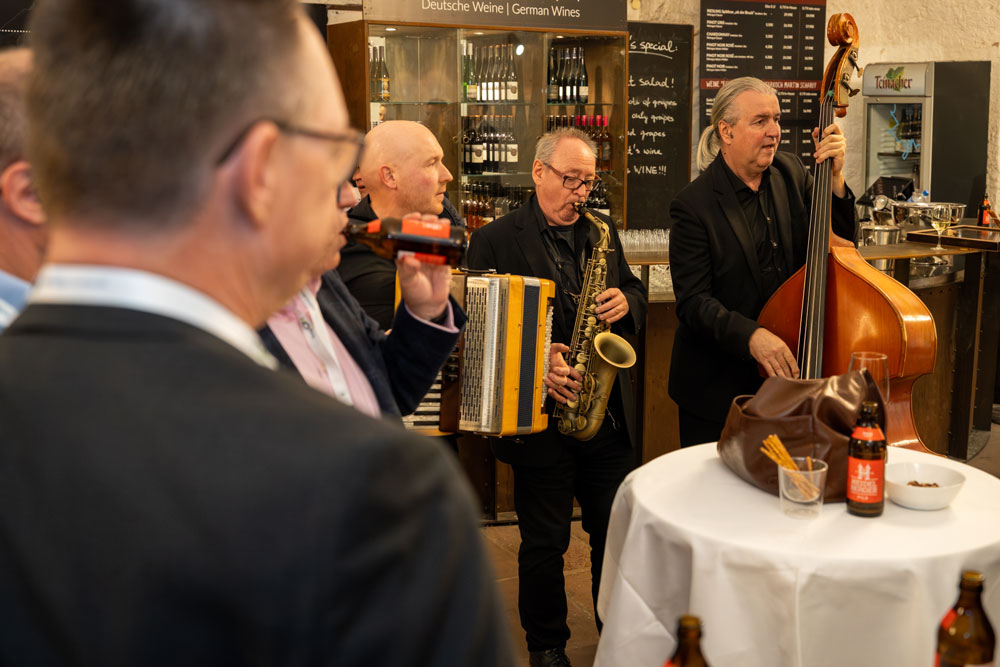 hsag-87 Eine kleine Jazzband spielt bei einer Indoor-Veranstaltung neben einem Tisch mit Getränken und Snacks.
